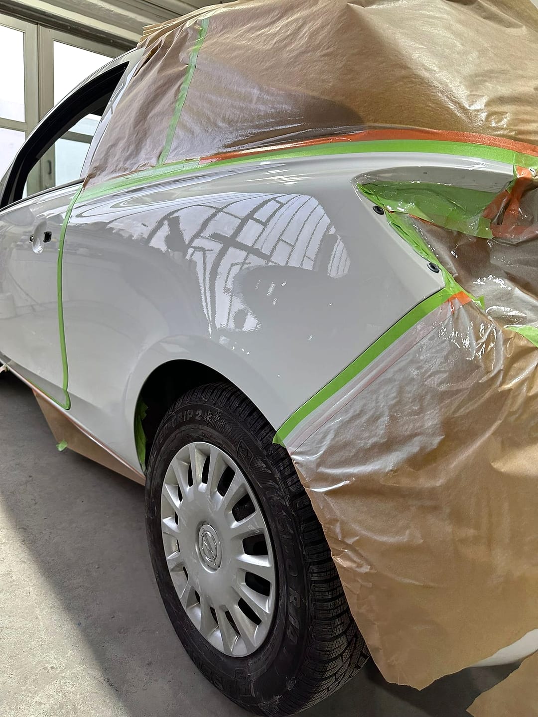 Weißes Fahrzeug mit Papier und Klebeband abgedeckt, nur das Seitenteil liegt zum Lackieren frei